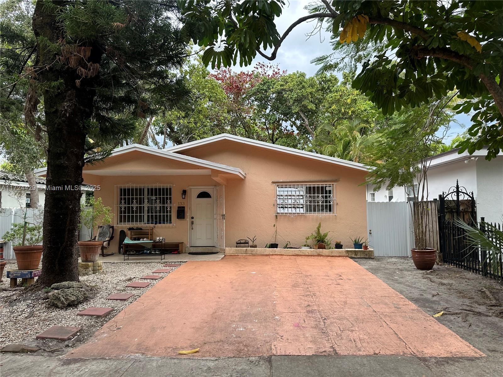 A peach-colored single-story house features a concrete driveway, security bars on windows, and mature trees — 133 NE 48th St, Miami FL 33137, MIAMI, FL