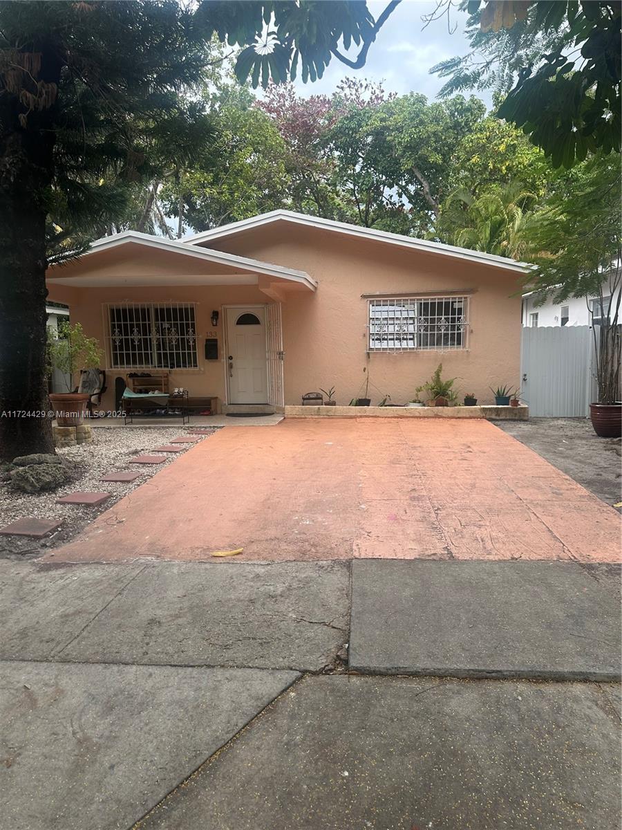 A single-story peach-colored house features a concrete driveway, security bars on windows, and mature trees — 133 NE 48th St, Miami FL 33137, MIAMI, FL