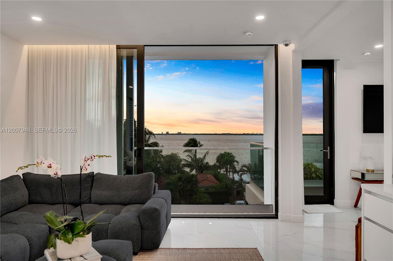 A living room features a large glass sliding door overlooking a sunset water view — 11 Century Ln, Miami Beach FL 33139, MIAMI BEACH, FL