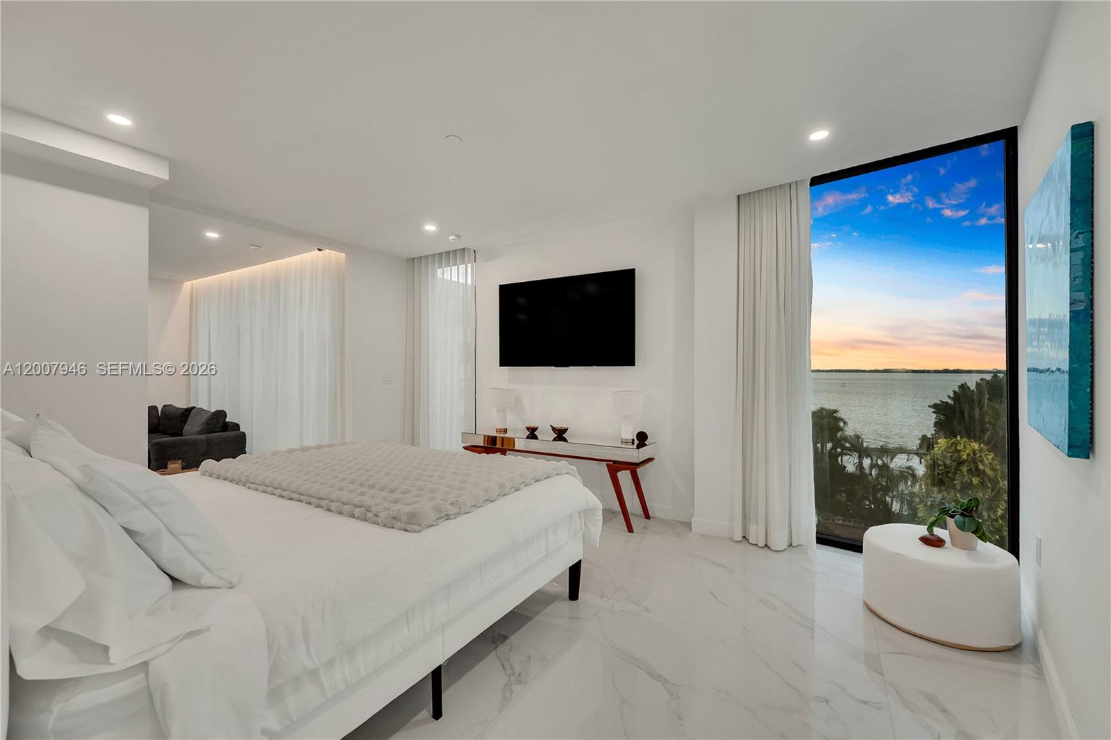 A modern bedroom features white marble floors, a wall-mounted television, and floor-to-ceiling windows overlooking water — 11 Century Ln, Miami Beach FL 33139, MIAMI BEACH, FL