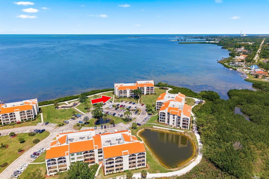 An aerial view shows several multi-story apartment buildings with orange roofs near a large bay — 302 MARINER DRIVE UNIT 302, TARPON SPRINGS, FL