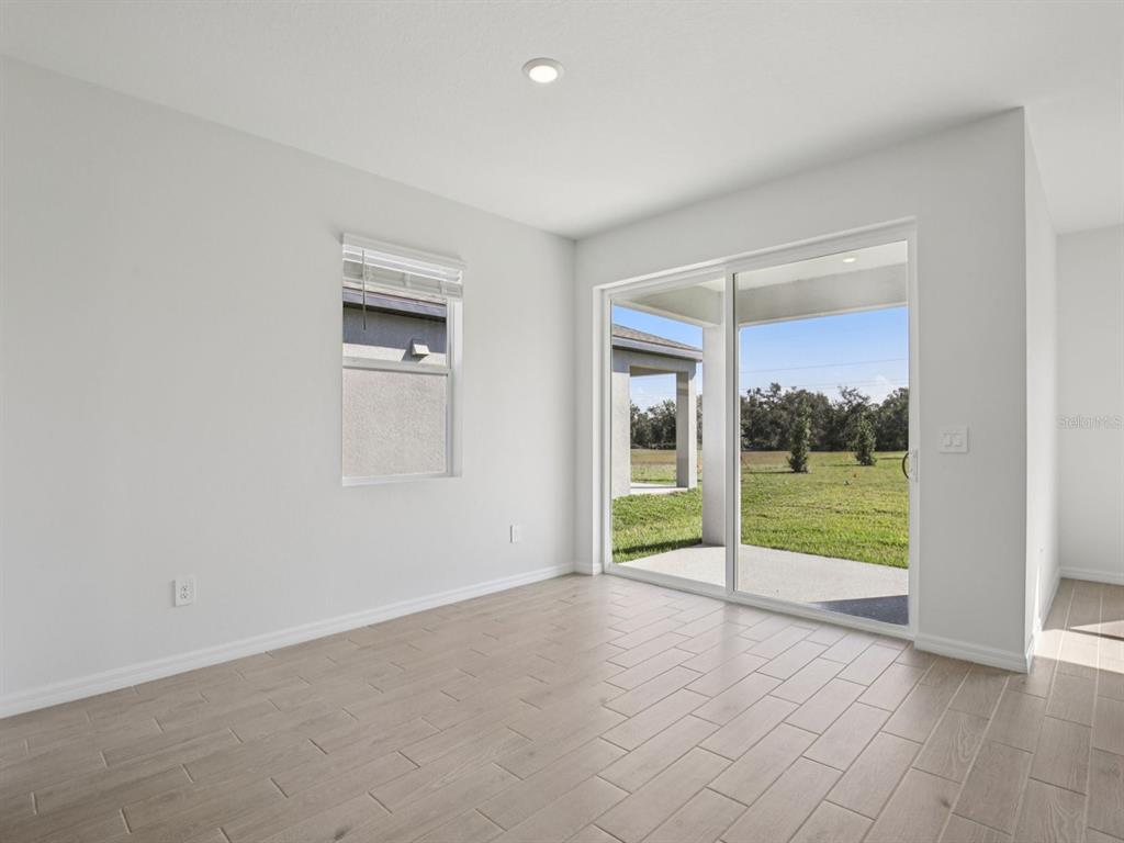An empty room with light wood-look tile flooring, a window, and sliding glass patio doors — 13314 SHELLMORE AVENUE, PALMETTO, FL