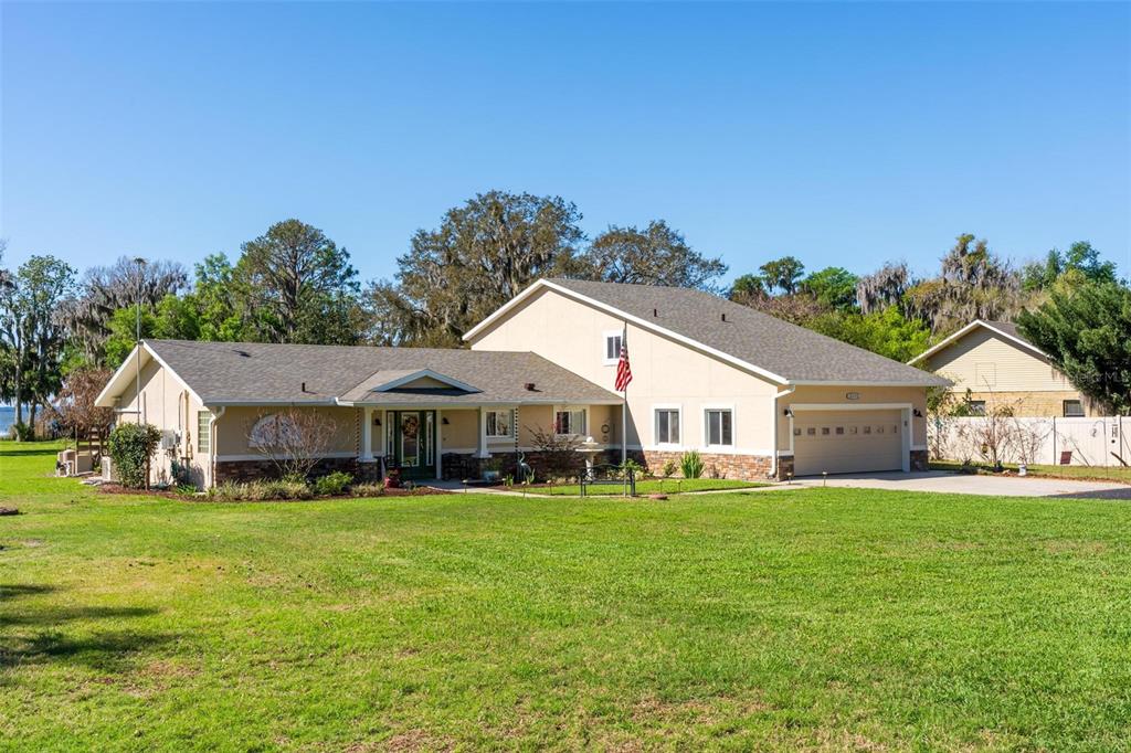 A grassy lawn leads to a line of Spanish moss-covered trees overlooking a lake — 10220 BUMBLEBEE LANE, LEESBURG, FL