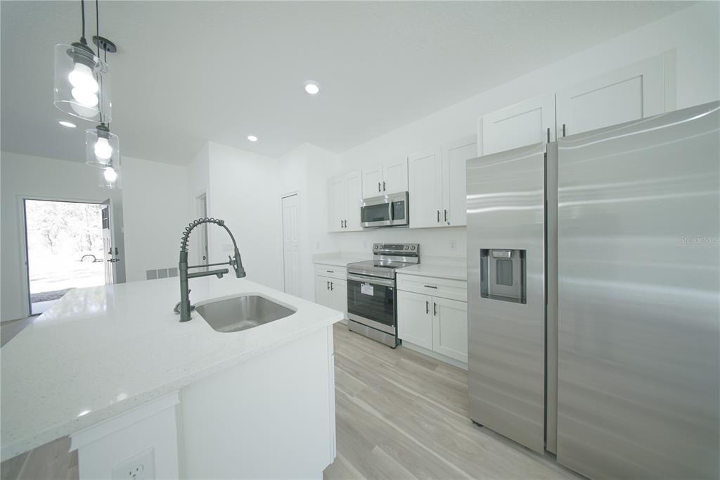 A modern kitchen features white cabinets, stainless steel appliances, a center island, and light flooring — 13753 SW 79TH TERRACE ROAD, OCALA, FL