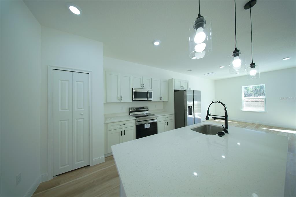 A modern kitchen features white cabinetry, a quartz island with a sink, and pendant lighting — 13753 SW 79TH TERRACE ROAD, OCALA, FL