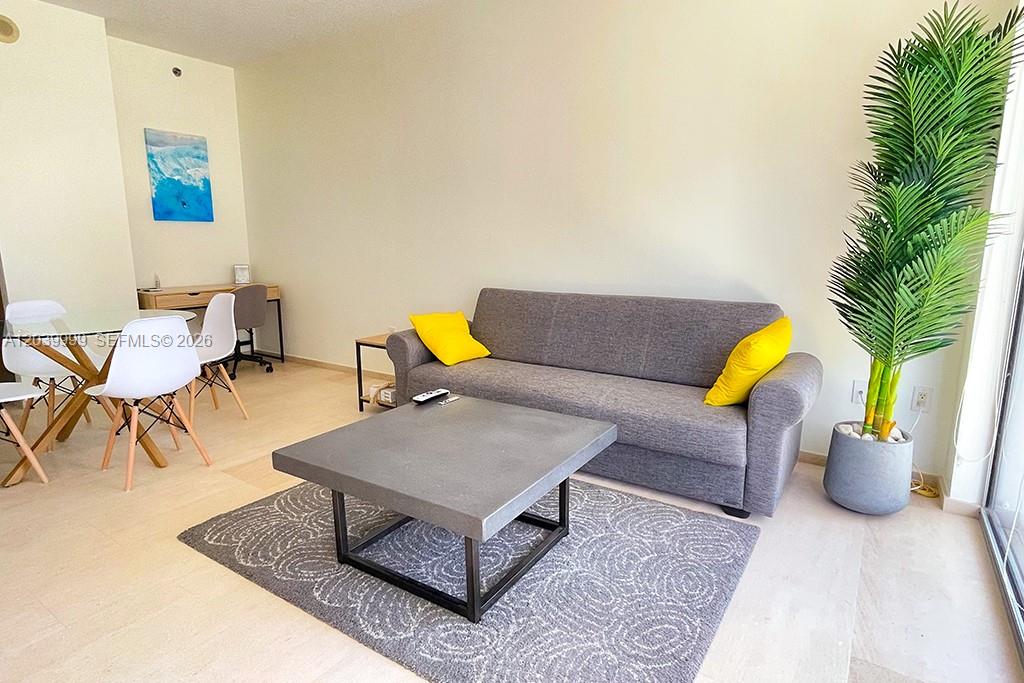 A living room features a gray sofa with yellow pillows, a coffee table, and a plant — 1050 Brickell Ave # 2208, Miami FL 33131, MIAMI, FL