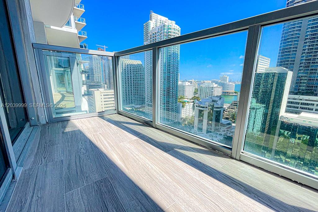 A high-rise balcony features wood-look tile flooring and glass railings overlooking a city skyline — 1050 Brickell Ave # 2208, Miami FL 33131, MIAMI, FL