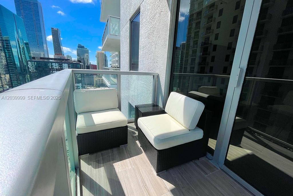 A balcony features two wicker chairs with white cushions and a view of city skyscrapers — 1050 Brickell Ave # 2208, Miami FL 33131, MIAMI, FL