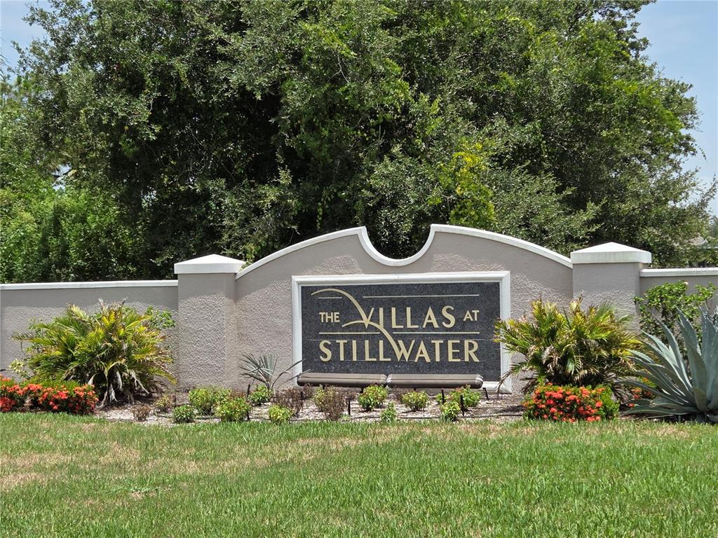 A beige stucco monument sign for The Villas at Stillwater sits amidst landscaped greenery — 13404 ABERCROMBIE DRIVE, ENGLEWOOD, FL