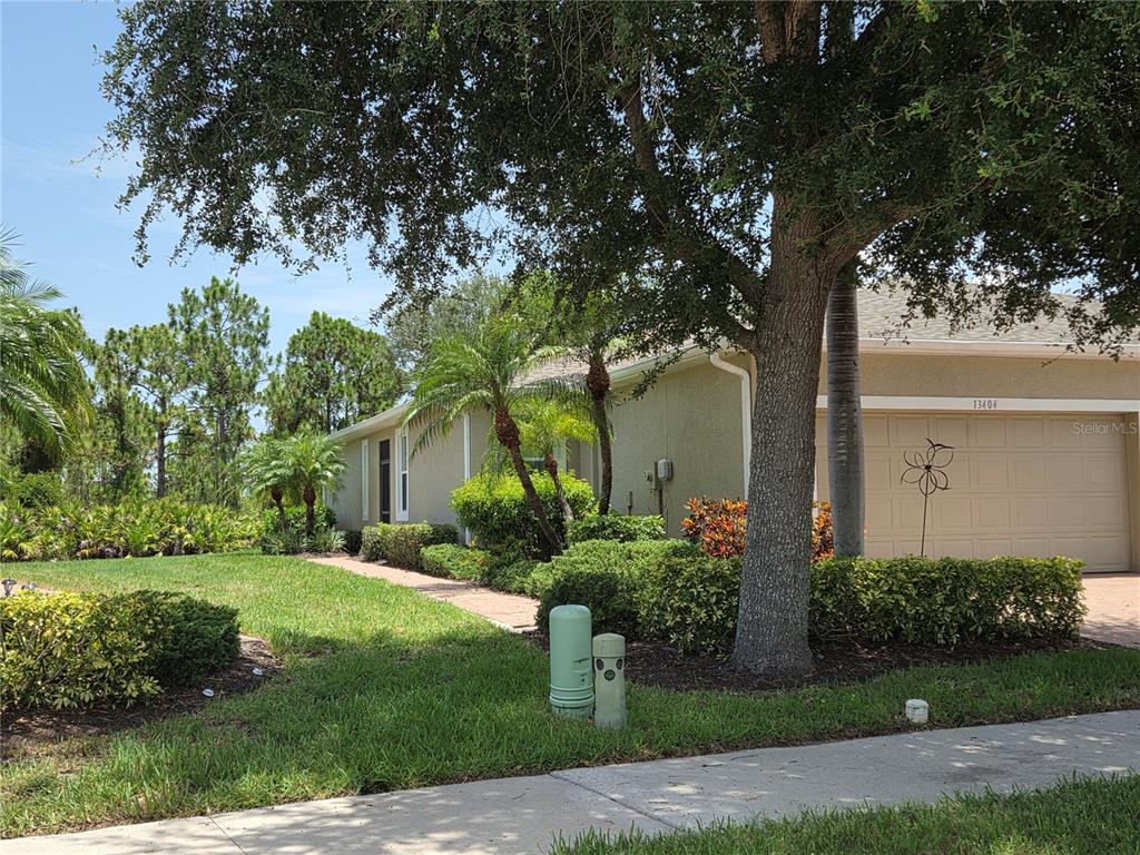 A single-story house with a tan stucco exterior, a two-car garage, and mature landscaping — 13404 ABERCROMBIE DRIVE, ENGLEWOOD, FL