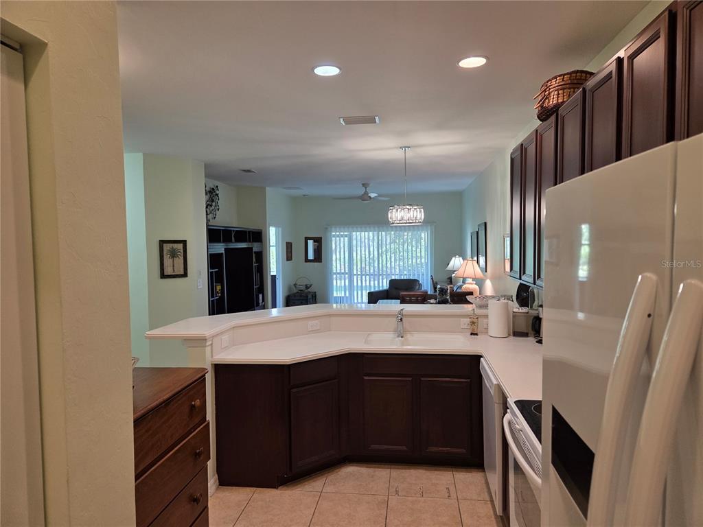 A kitchen with dark wood cabinets, white countertops, and a view into the living area — 13404 ABERCROMBIE DRIVE, ENGLEWOOD, FL
