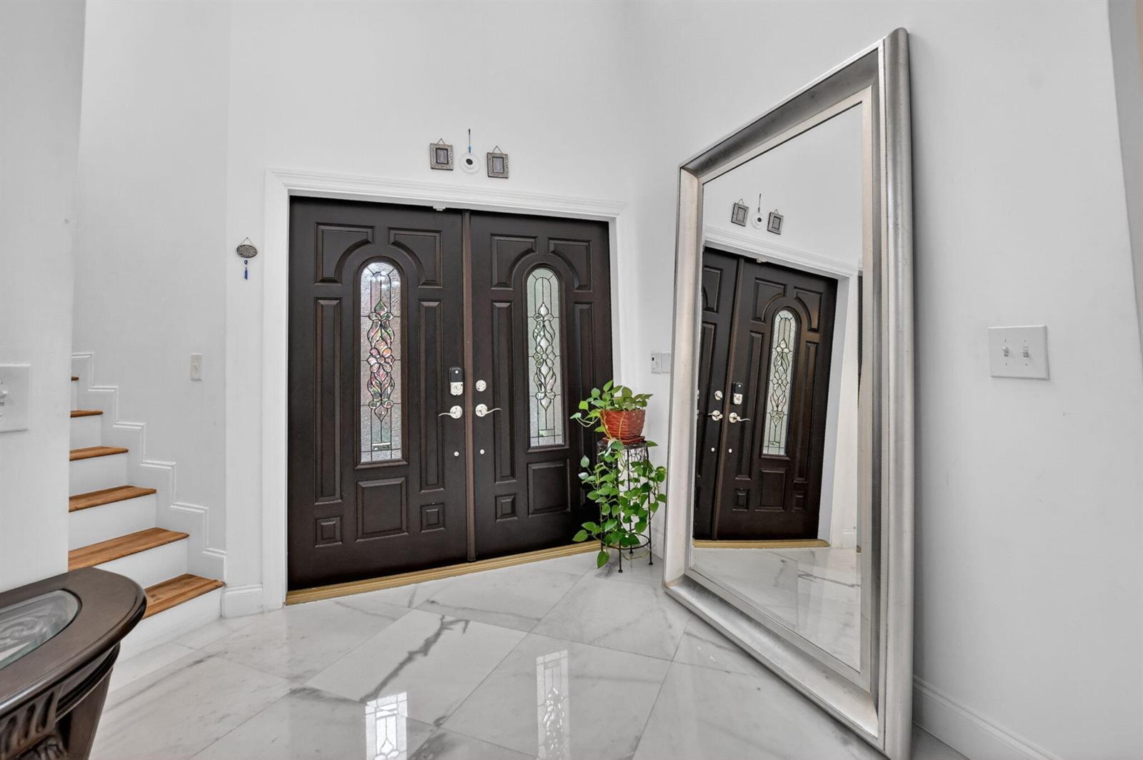 A bright entryway features double dark wood doors, marble flooring, a large floor mirror, and stairs — 23260 Mirabella Circle N, Boca Raton FL 33433, BOCA RATON, FL