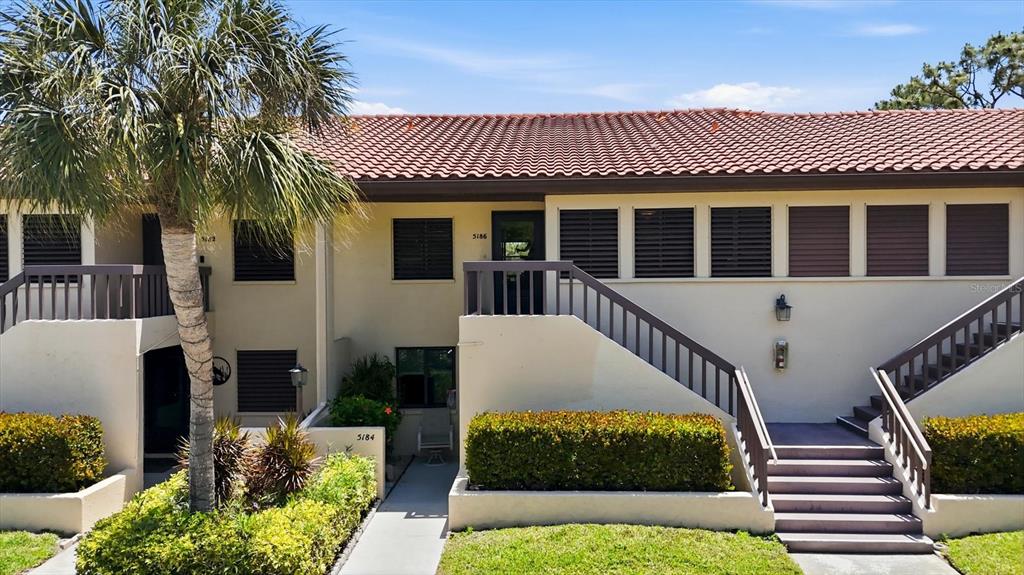 A two-story residential building features a palm tree, exterior stairs, and dark-shuttered windows — 5186 LAKE VILLAGE DRIVE UNIT 90, SARASOTA, FL