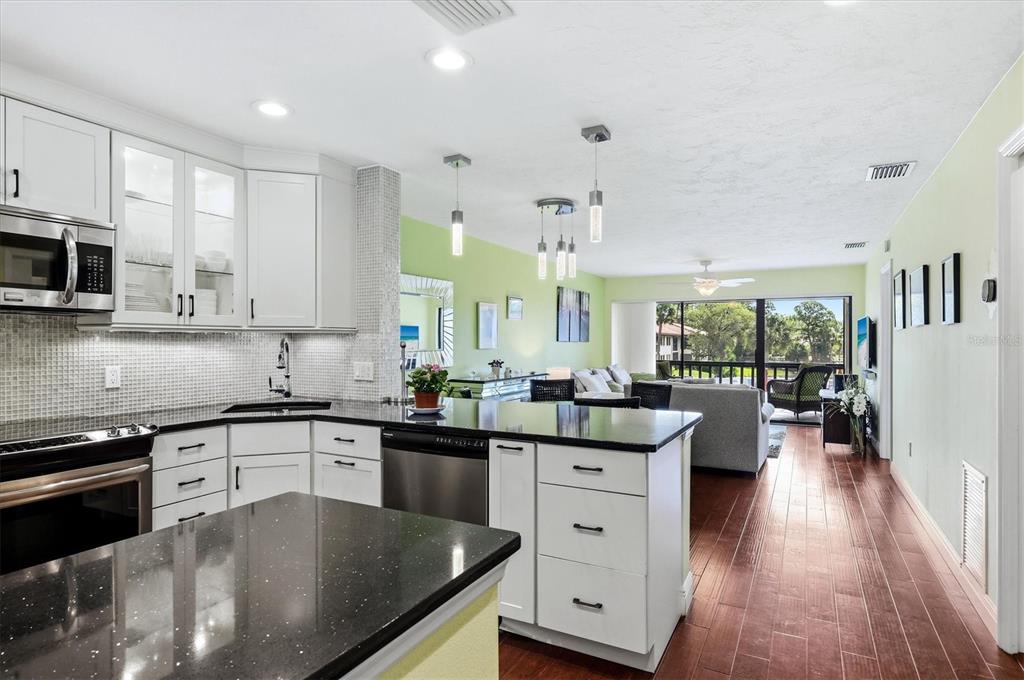 A kitchen with white cabinets and black countertops opens into a living area with balcony views — 5186 LAKE VILLAGE DRIVE UNIT 90, SARASOTA, FL