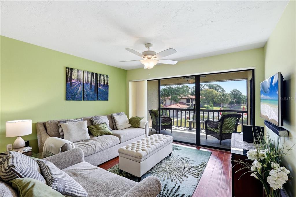 A living room with light green walls, a gray sofa, and a sliding glass door — 5186 LAKE VILLAGE DRIVE UNIT 90, SARASOTA, FL
