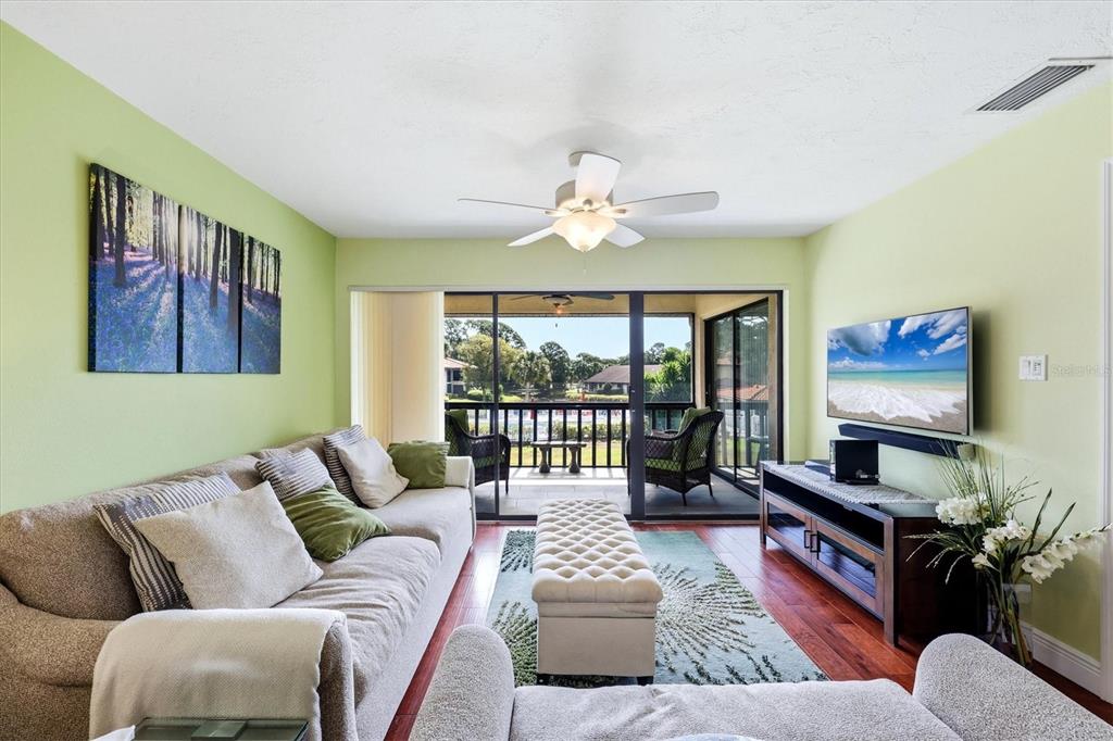 A living room with light green walls, a beige sofa, and sliding doors to a balcony — 5186 LAKE VILLAGE DRIVE UNIT 90, SARASOTA, FL