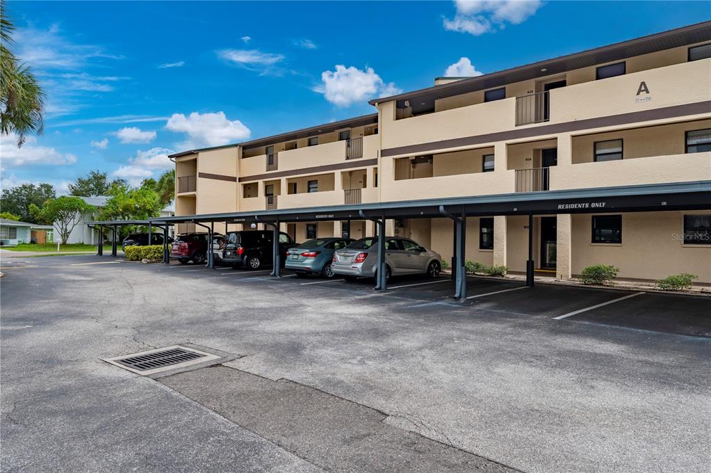 A multi-story apartment building with covered parking spaces in front under a blue sky — 2395 HARBOR BOULEVARD UNIT 310, PORT CHARLOTTE, FL