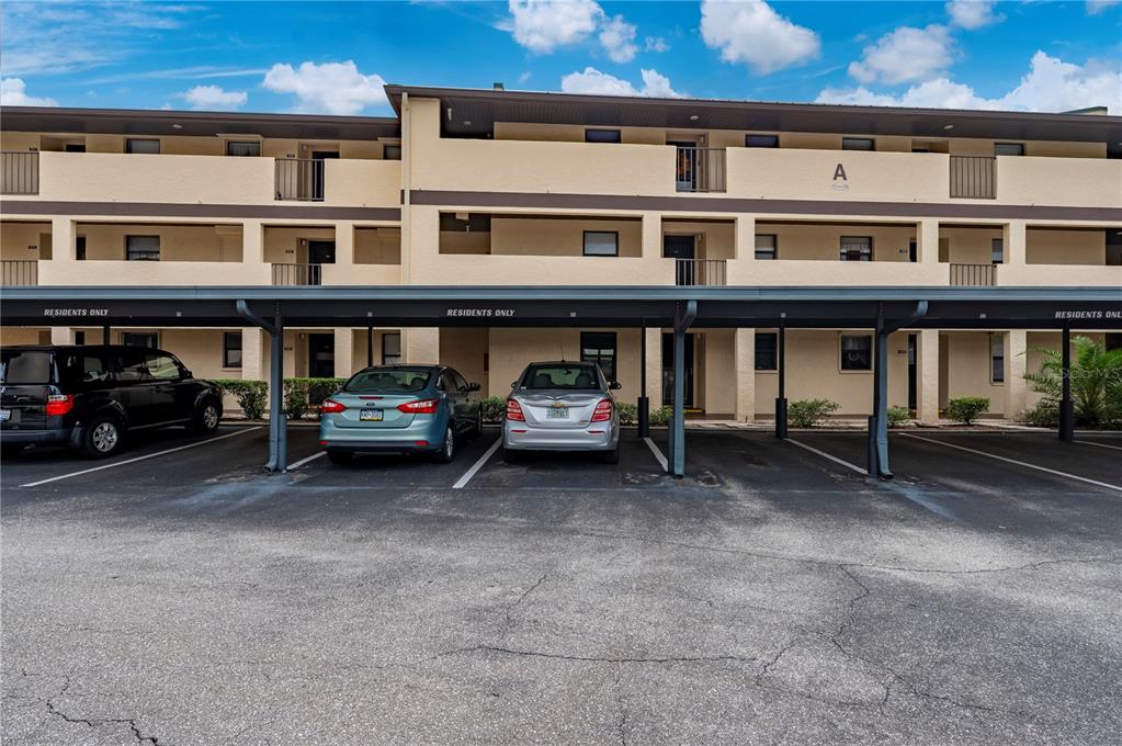 A three-story apartment building with a covered parking area for residents in the foreground — 2395 HARBOR BOULEVARD UNIT 310, PORT CHARLOTTE, FL