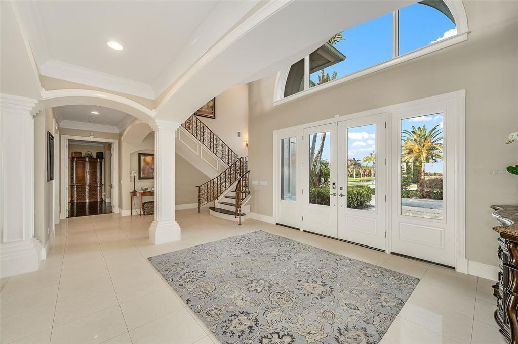 A bright foyer features a large area rug, a staircase, and double glass entry doors — 281 LANSING ISLAND DRIVE, INDIAN HARBOUR BEACH, FL