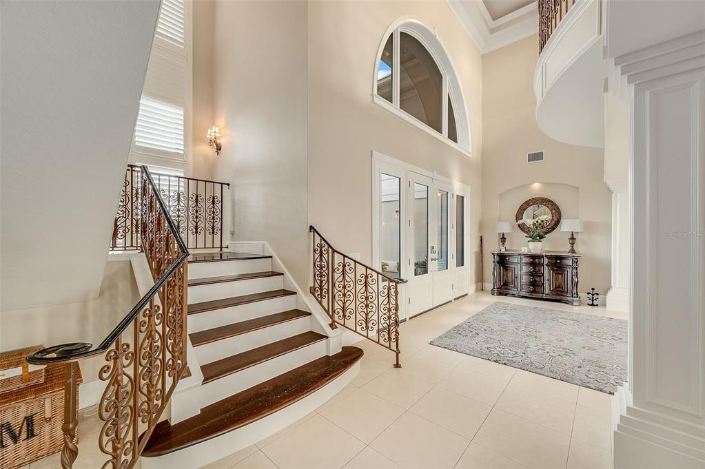 A grand foyer features a curved staircase with ornate metal railings and tile flooring — 281 LANSING ISLAND DRIVE, INDIAN HARBOUR BEACH, FL