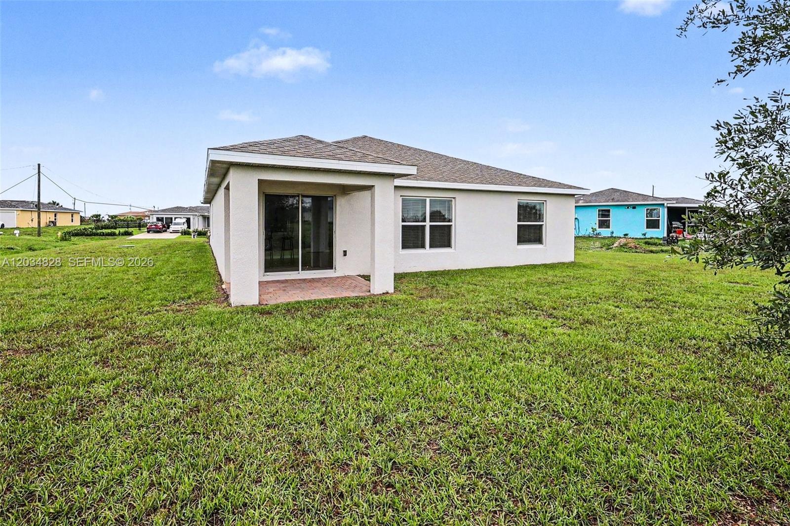 The rear exterior of a single-story house features a covered patio and a grassy yard — 9045 Maywood Cir, La Belle FL 33935, LA BELLE, FL