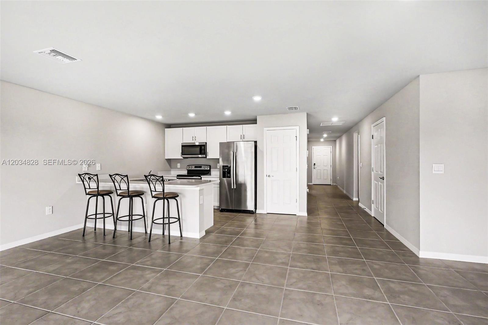 A kitchen with white cabinets, stainless steel appliances, and a breakfast bar with three stools — 9045 Maywood Cir, La Belle FL 33935, LA BELLE, FL