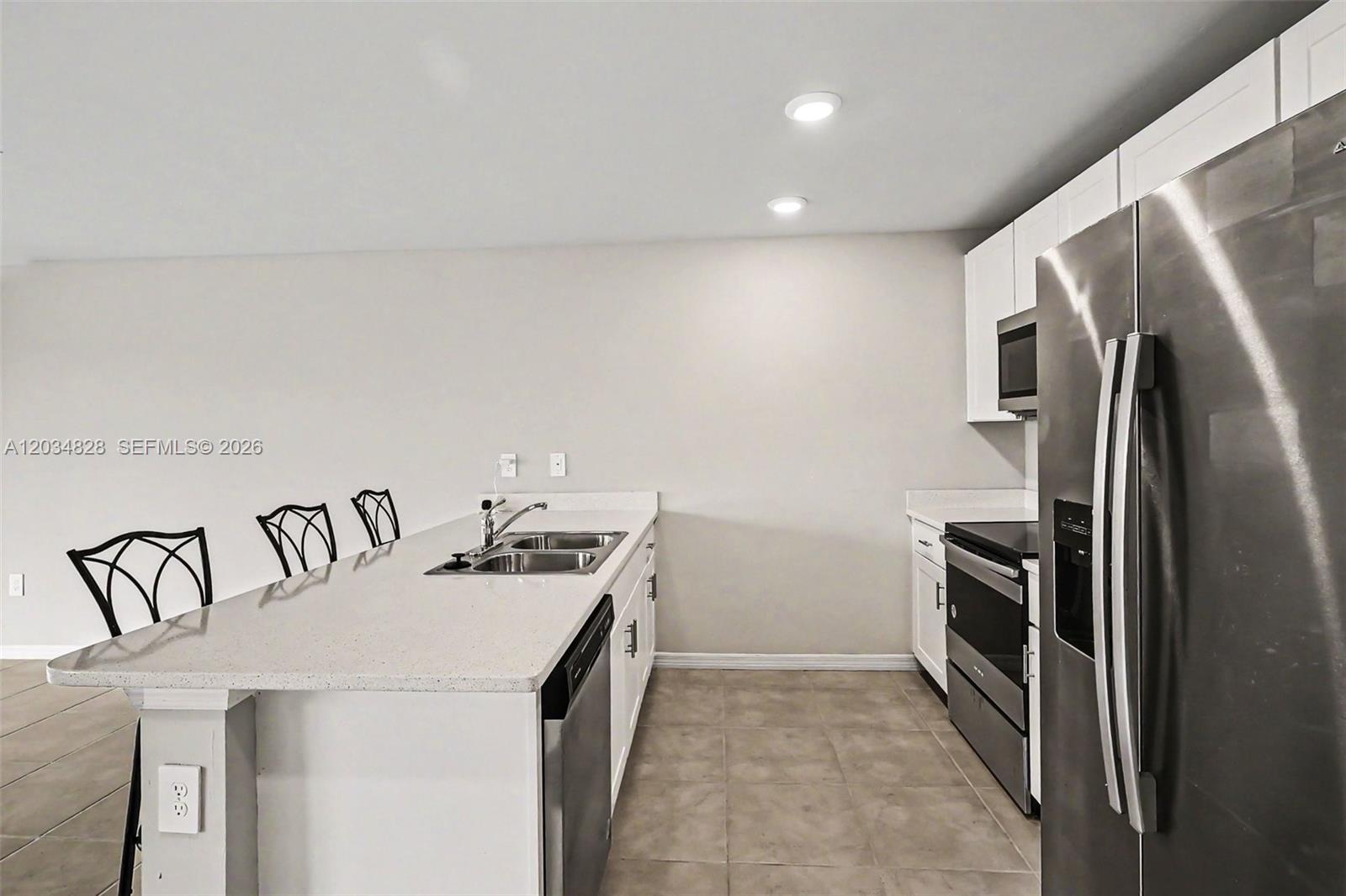 A kitchen features white cabinets, stainless steel appliances, a quartz island, and tile flooring — 9045 Maywood Cir, La Belle FL 33935, LA BELLE, FL