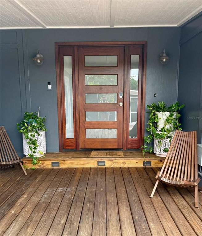 A wooden front door with glass panels is centered on a deck with two chairs — 3012 GRAND VIEW AVENUE, CLEARWATER, FL