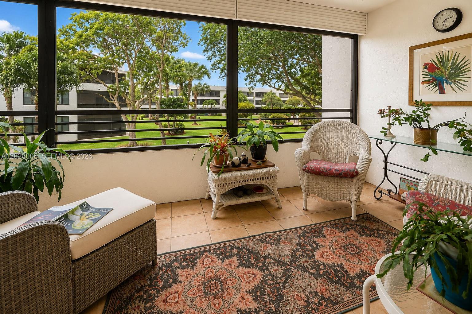 A sunroom features wicker furniture, a patterned area rug, and large windows overlooking a courtyard — 1450 Sheridan St # 13, Hollywood FL 33020, HOLLYWOOD, FL