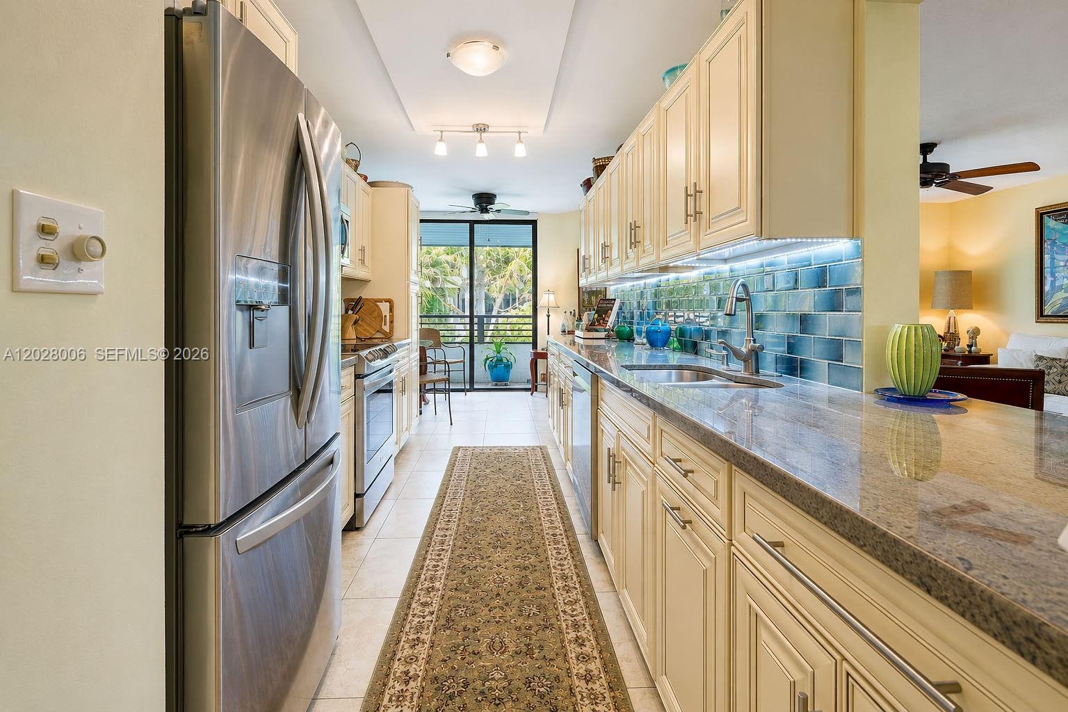 A galley kitchen features cream cabinets, granite countertops, a blue tile backsplash, and stainless appliances — 1450 Sheridan St # 13, Hollywood FL 33020, HOLLYWOOD, FL
