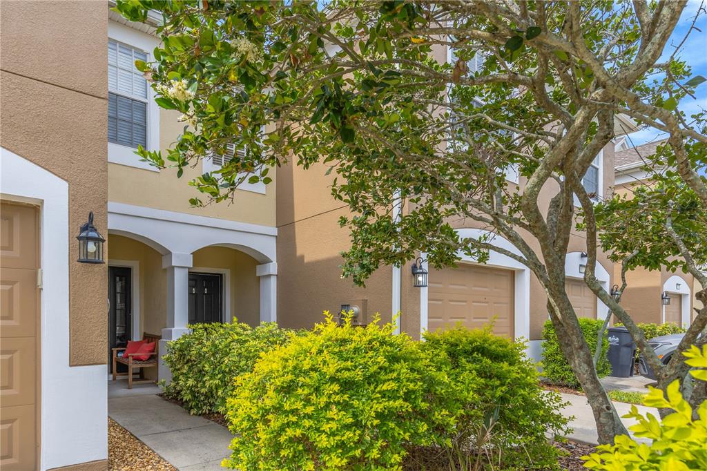 A two-story townhouse exterior with a tan stucco facade, a small porch, and a garage — 10135 POST HARVEST DRIVE, RIVERVIEW, FL