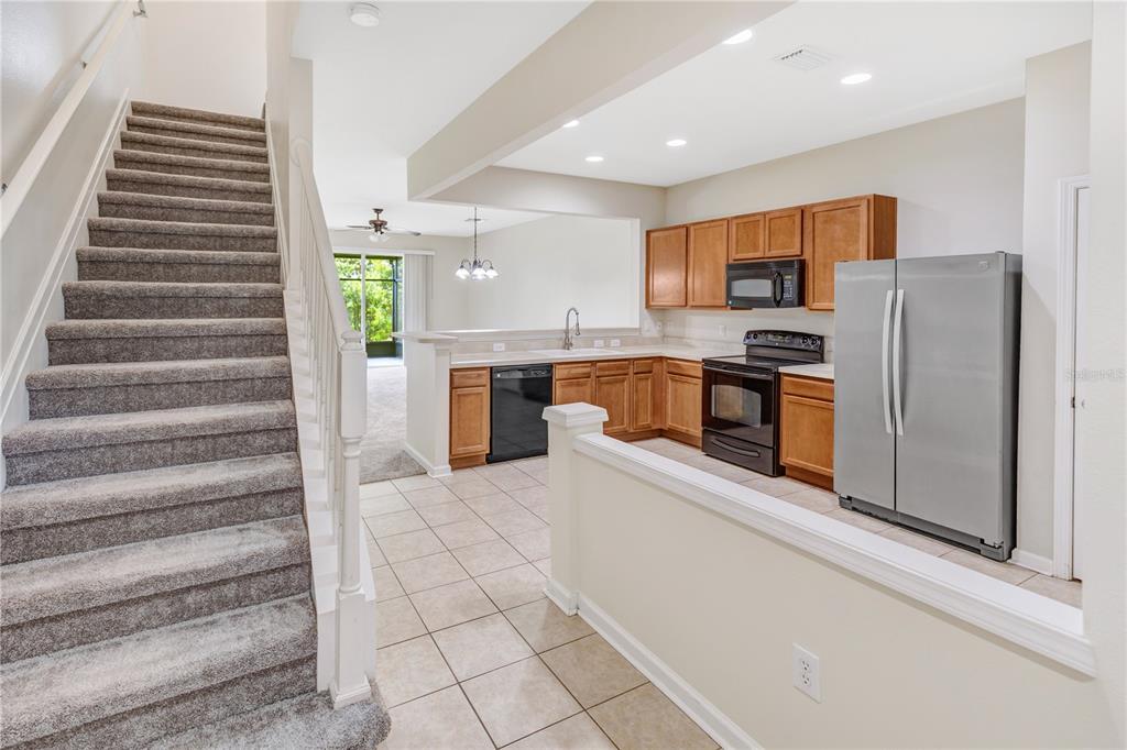 A kitchen with wood cabinets and stainless steel appliances sits next to a carpeted staircase — 10135 POST HARVEST DRIVE, RIVERVIEW, FL