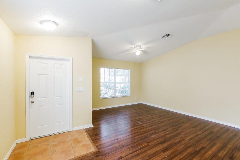 An empty room with light yellow walls, dark wood flooring, a ceiling fan, and front door — HOLLYWOOD, FL