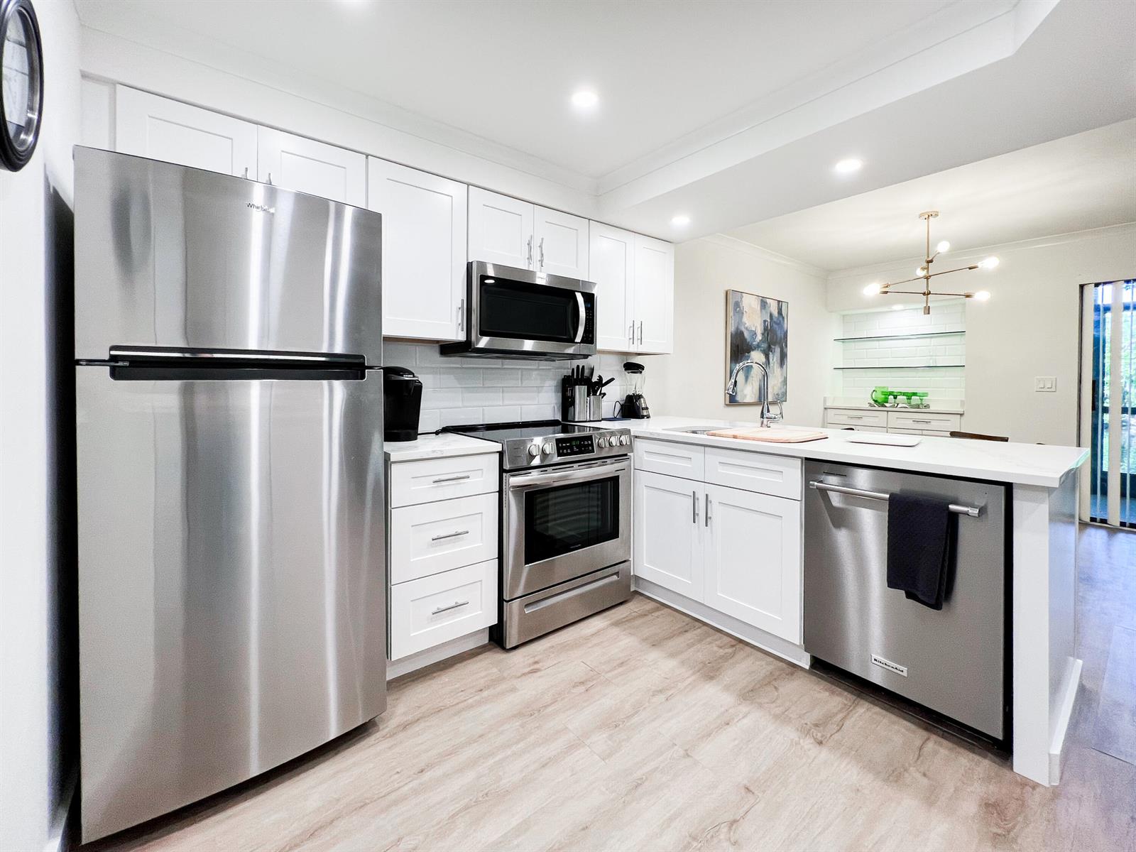 A kitchen featuring white cabinets, stainless steel appliances, and light wood-look flooring — 1605 S Us Highway 1 # C103, Jupiter FL 33477, JUPITER, FL