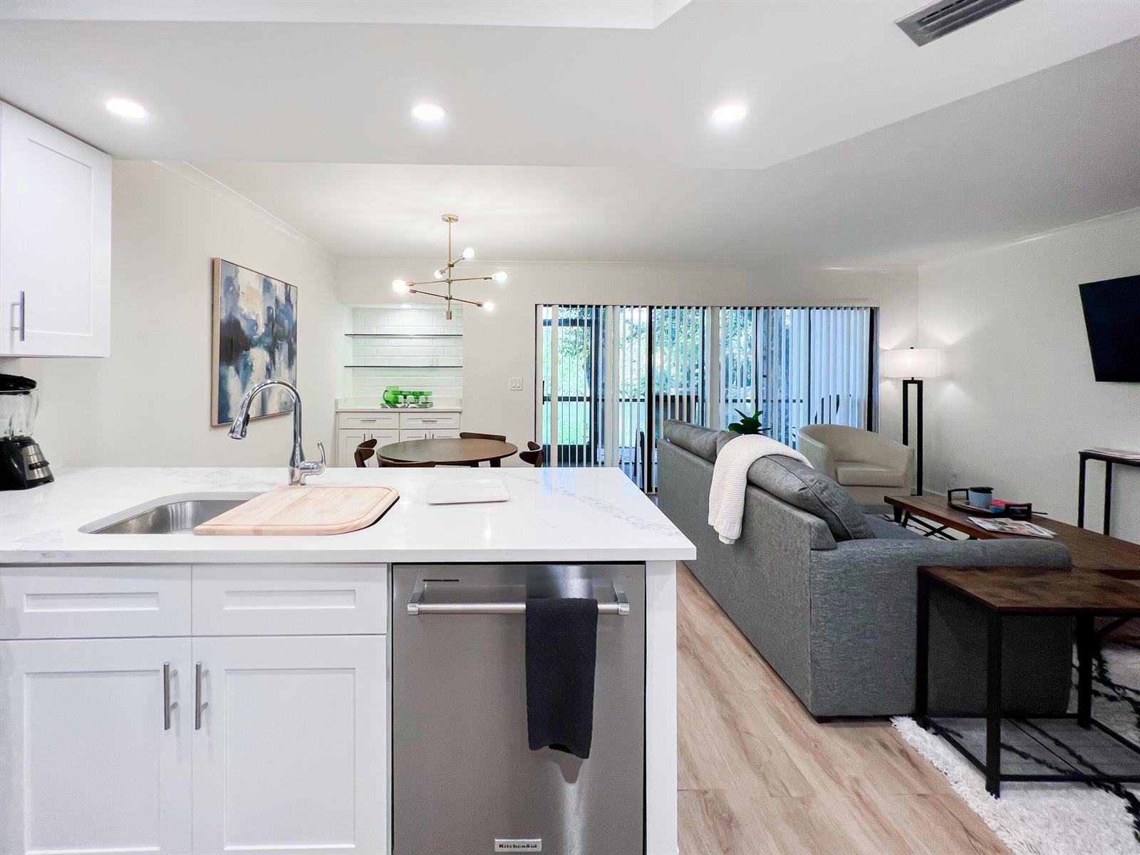 A modern kitchen with white cabinets and a stainless dishwasher overlooks a living room area — 1605 S Us Highway 1 # C103, Jupiter FL 33477, JUPITER, FL