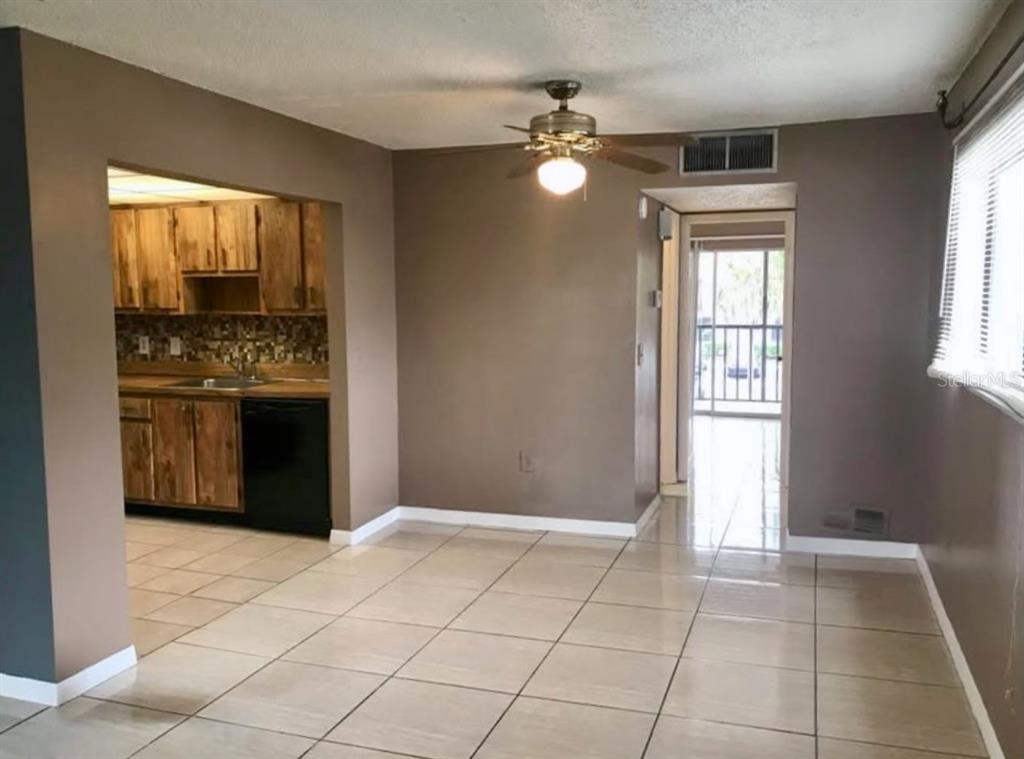 A dining area with tile flooring leads to a kitchen with wood cabinets and a balcony — 2565 OAK PARK WAY UNIT 213, ORLANDO, FL