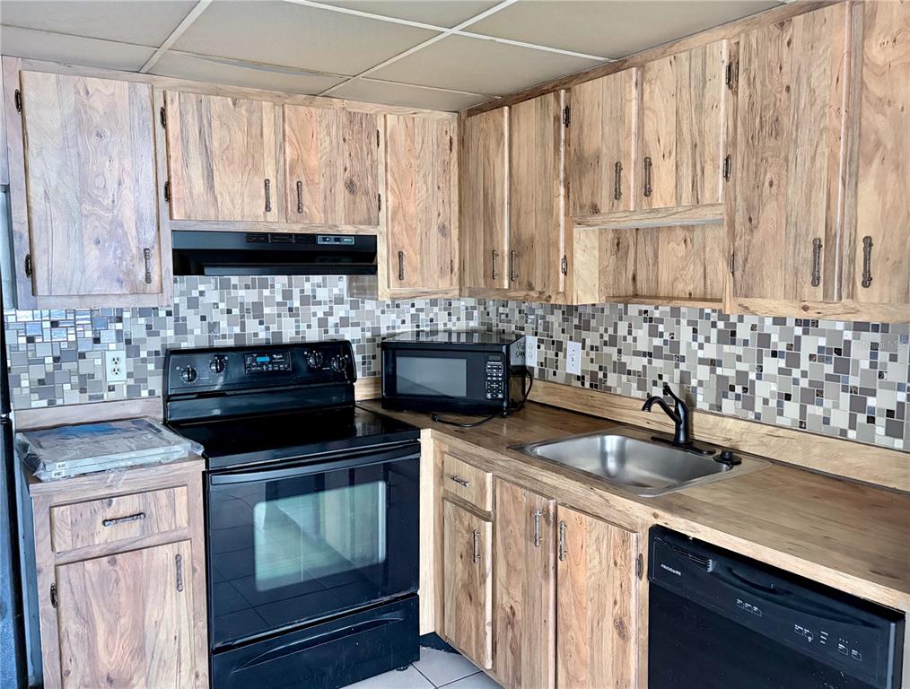 A kitchen features wood-grain cabinets, a tiled backsplash, black appliances, and a stainless steel sink — 2565 OAK PARK WAY UNIT 213, ORLANDO, FL