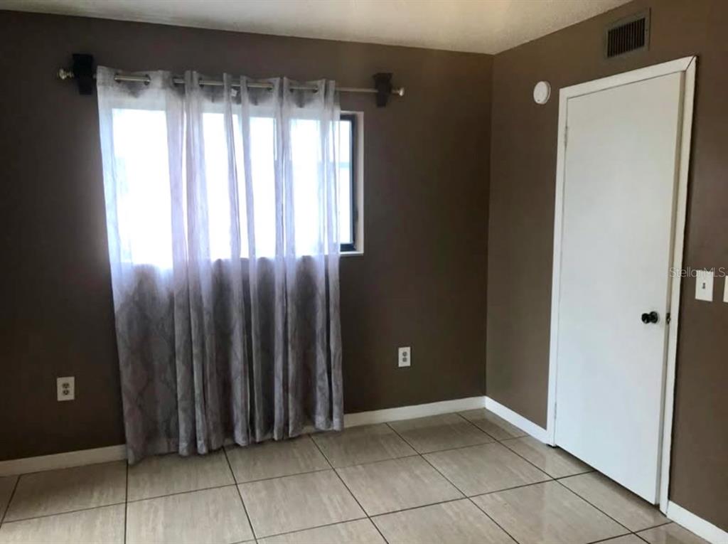 A bedroom features brown walls, tiled flooring, a window with sheer curtains, and a white door — 2565 OAK PARK WAY UNIT 213, ORLANDO, FL
