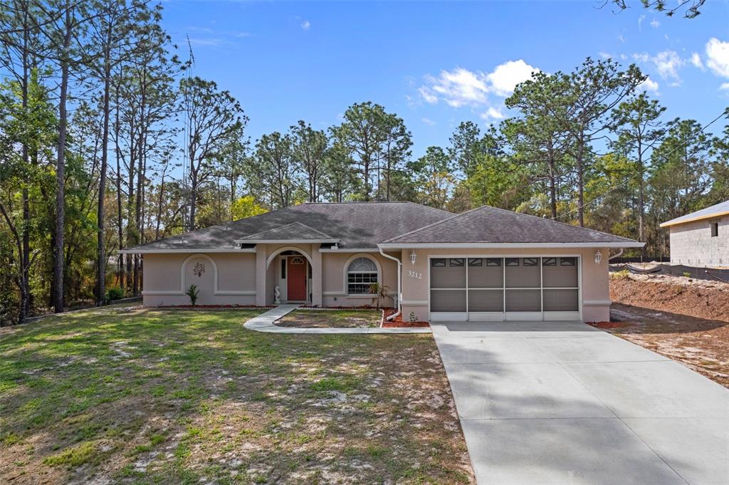 A single-story house with a beige stucco exterior, a red front door, and a garage — 3212 W CAMILO DRIVE, CITRUS SPRINGS, FL