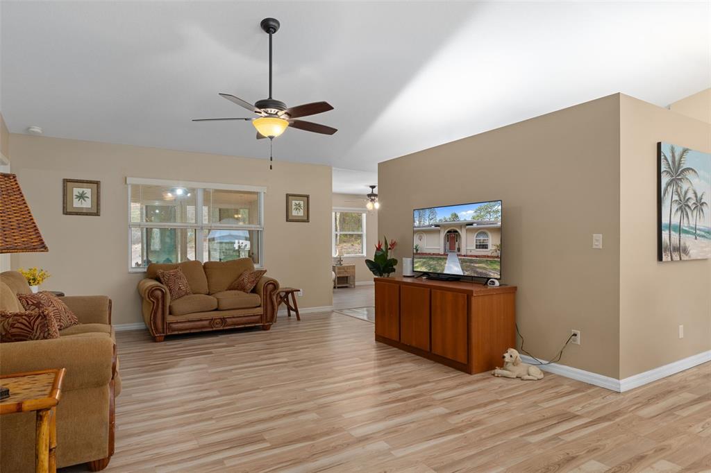 A living room features light wood-look flooring, tan walls, a ceiling fan, and a television — 3212 W CAMILO DRIVE, CITRUS SPRINGS, FL