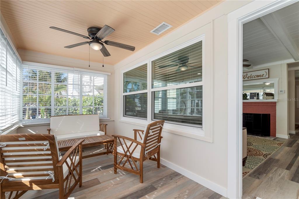 A sunroom features wood-look flooring, a ceiling fan, and a view into an adjacent room — 105 21ST AVENUE, ST PETE BEACH, FL
