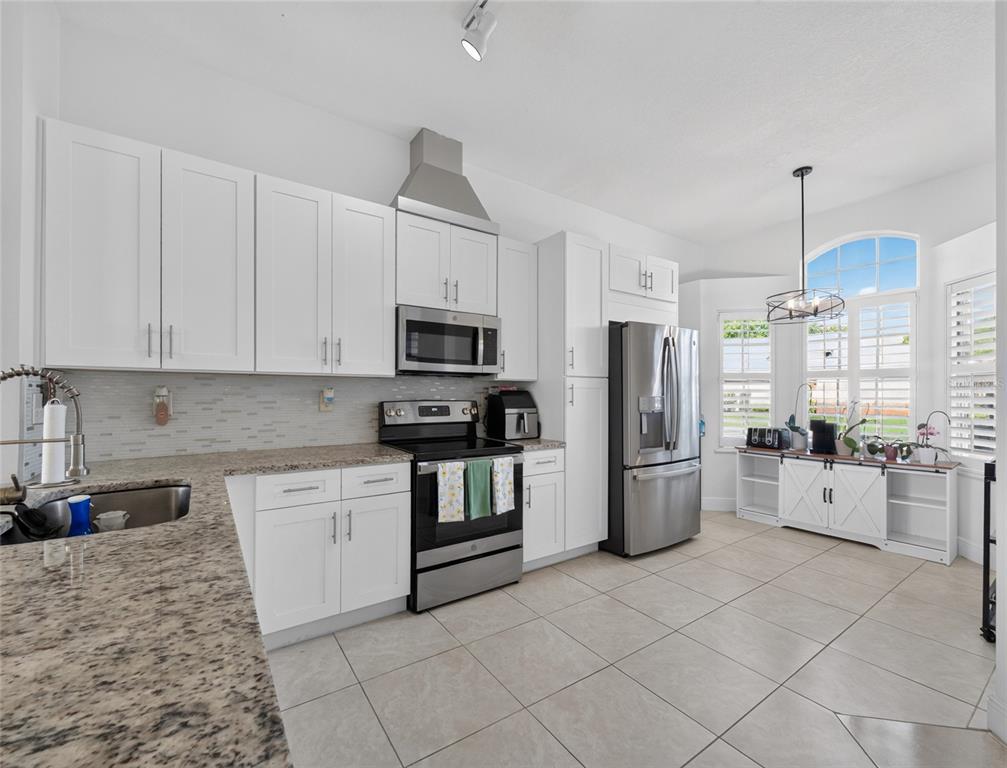 A kitchen features white cabinetry, stainless steel appliances, granite countertops, and a dining nook area — 14435 WINDCHIME LANE, ORLANDO, FL