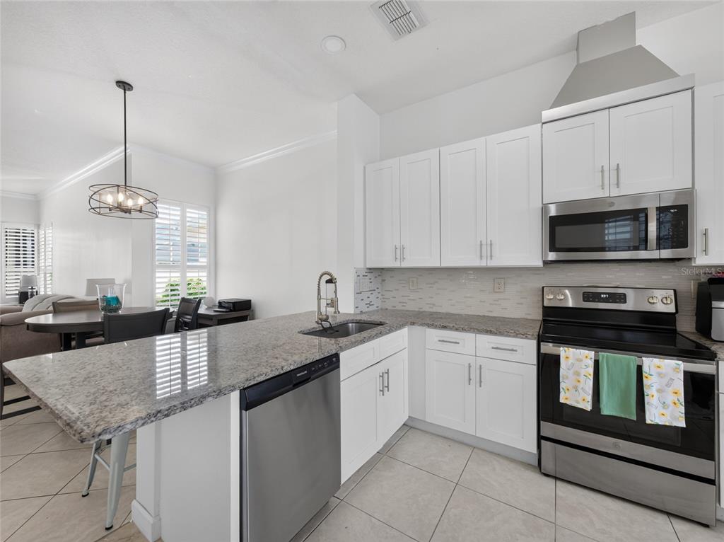 A kitchen features white cabinets, granite countertops, stainless steel appliances, and an adjacent dining area — 14435 WINDCHIME LANE, ORLANDO, FL