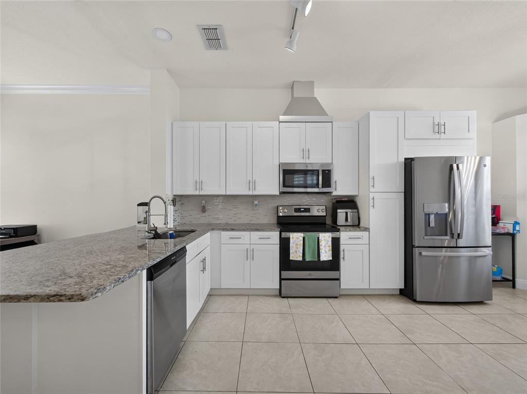 A kitchen features white cabinets, stainless steel appliances, and a granite-topped peninsula island — 14435 WINDCHIME LANE, ORLANDO, FL