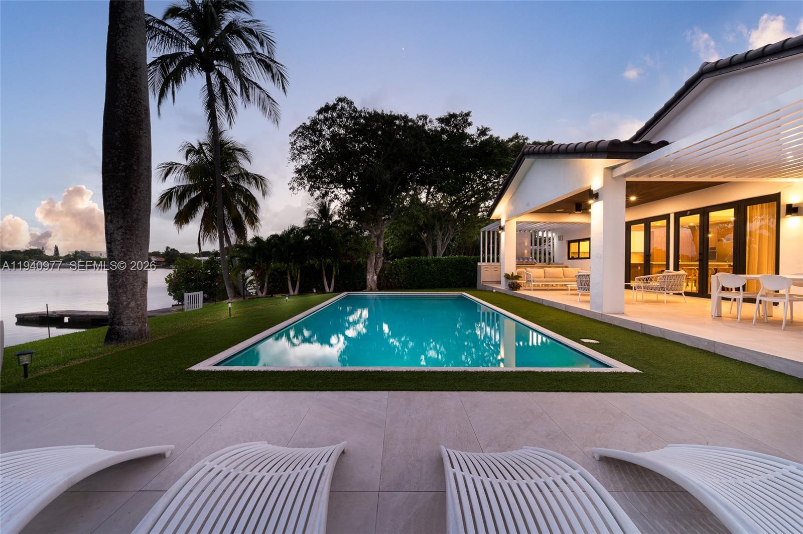 A rectangular swimming pool sits on a lawn beside a house with a covered patio — 2560 NE 199th St, Miami FL 33180, MIAMI, FL