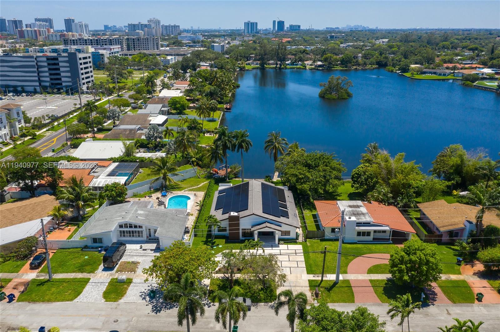 An aerial view shows three houses with pools and solar panels situated beside a lake — 2560 NE 199th St, Miami FL 33180, MIAMI, FL