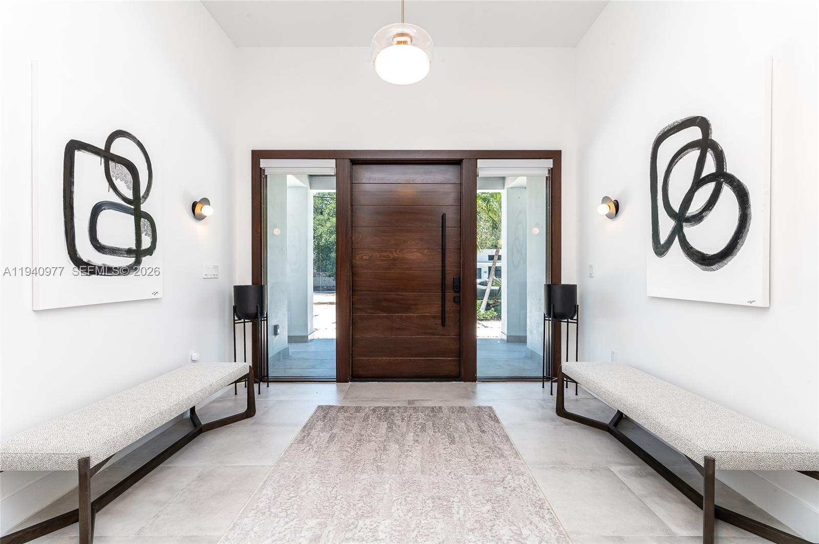 A modern entryway features a wooden door, two benches, abstract wall art, and tile flooring — 2560 NE 199th St, Miami FL 33180, MIAMI, FL