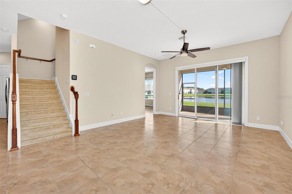 An open living area features tan tile flooring, a carpeted staircase, and sliding glass doors — 2101 PAINTER LANE, KISSIMMEE, FL