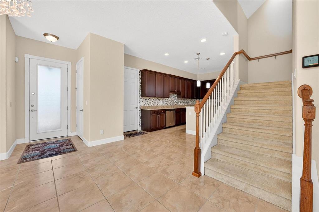 An entryway with tile flooring leads to a kitchen with dark cabinets and a staircase — 2101 PAINTER LANE, KISSIMMEE, FL