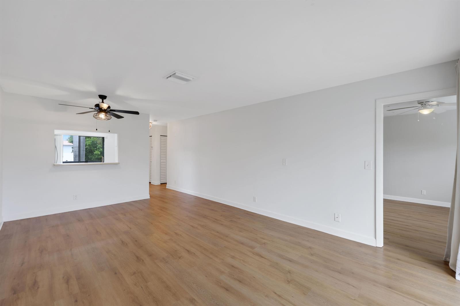 An empty room with light wood-look flooring, white walls, a ceiling fan, and a pass-through window — 3275 Frederick Boulevard # 17, Delray Beach FL 33483, DELRAY BEACH, FL